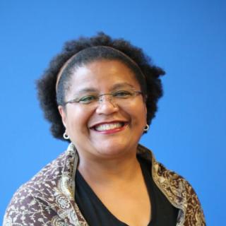 An African American woman wearing glasses and smiling against a blue background.