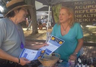 Photo of a woman handing another woman flyers at a farmer's market.