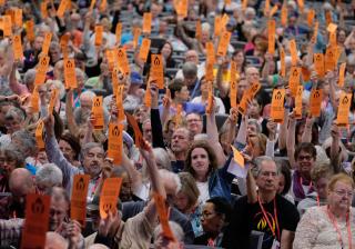 a large indoor gathering holds up orange paper voting cards