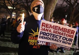 protester holding a candle and a sign that reads "remember Jan 7, senators, protect our democracy now"