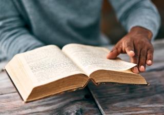 Stock photo of brown hands turning pages of an old book that looks like the bible. 