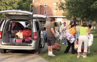 Family moving children into college, with the back of an SUV filled with boxes and clothes.