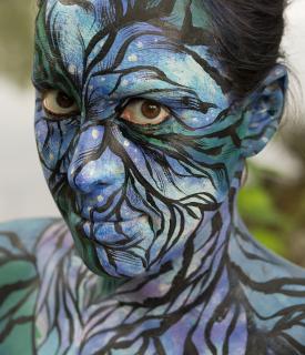 Zoomorphic #5: photograph of a woman with her face, neck, and shoulders painted with black lines and blues and greens.