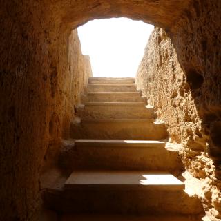 photograph of rough hewn stone stairs, looking up from the bottom into the light.