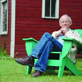 UU Poet Ted Kooser sitting in a chair on a lawn