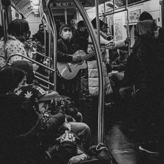 A man on a subway train masked and playing a guitar while onlookers watch.
