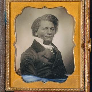A lithograph of a Black man in a suit. The lithograph is framed by a golden-brown booklet.