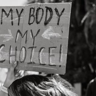 A black-and-white photo of a person holding up a sign that says "My body my choice" at a reproductive rights demonstration.