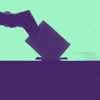 A hand places a paper ballot into a voting box.