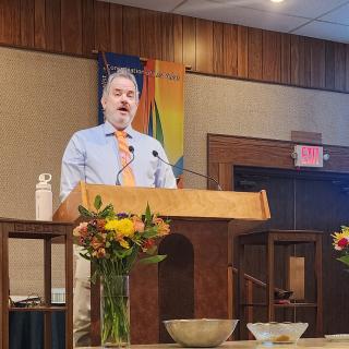 A person speaks at a podium on stage during a congregational service.