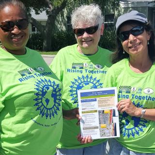 three women in green Rising Together tee shirts holding an outreach sheet