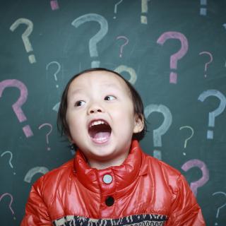 Asian child in front of chalkboard which has question marks on it.