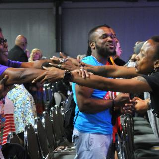 Ndidi Achebe, left, and Ebonie Remsey link arms during the closing worship as the gathering sang “I need you to survive.”