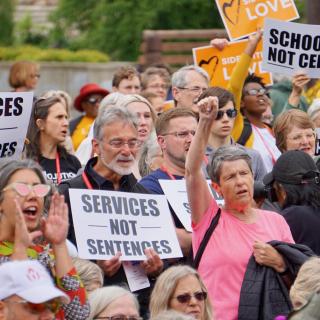 Protesters hold signs "Services not Sentences" and "Schools not Cells" at the General Assembly public witness event