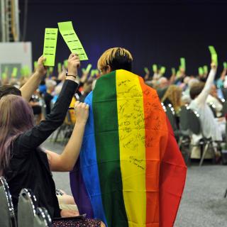 Youth sign a rainbow flag as delegates raise voting cards at 2016 GA