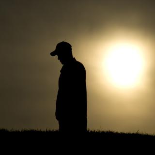 Silhouette of man looking down with sunset in background.