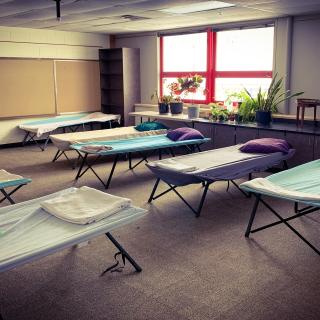Clean sheets in shades of purple, white, and light blue stretch appealingly over rows of cots at Shawnee Mission Unitarian Universalist Church, ready for those without shelter. 
