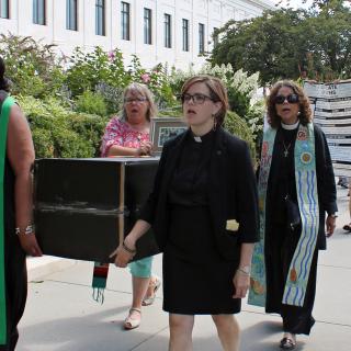 Interfaith clergy (including Unitarian Universalist the Rev. Robin Tanner, center) carry a cardboard coffin while leading a procession to protest attempts to repeal the ACA, Washington, D.C., on July 25, 2017.