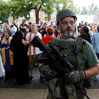 A member of a white supremacist militia stands in front of religious leaders, including UUA President Susan Frederick-Gray, who gathered to protest a rally of neo-Nazis and other white supremacists in Charlottesville, Virginia, on August 12, 2017. 