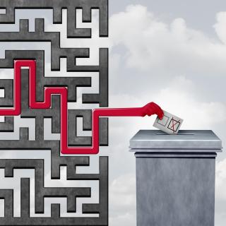 Stock image depicting a hand moving through a maze to get to a ballot box, symbolizing voting challenges, election problems, and voter suppression.