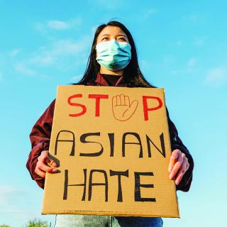 Stock photo of Asian person holding a sign saying "STOP ASIAN HATE" wearing a mask