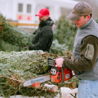 Man trimming bottom off of a christmas tree with a chainsaw