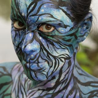 Zoomorphic #5: photograph of a woman with her face, neck, and shoulders painted with black lines and blues and greens.