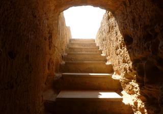 photograph of rough hewn stone stairs, looking up from the bottom into the light.