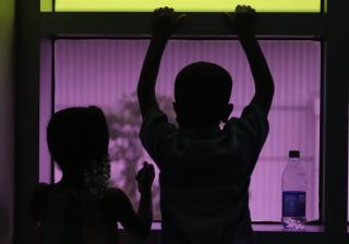 The silhouette of two young children in front of a purple-hued window.