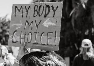 A black-and-white photo of a person holding up a sign that says "My body my choice" at a reproductive rights demonstration.