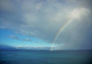 A rainbow connecting the blue sea to big, white clouds in a blue sky.