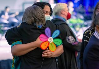 Rev. Gianni Fogliano, the UUA’s manager and strategist for Equity, Belonging, and Change, holds an Article II Shared Values flower while embracing former UUA President Susan Frederick-Gray at General Assembly 2023.