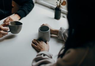 Focus on the hands of two people who are at a table drinking coffee