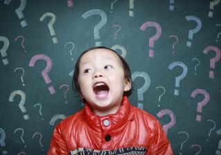 Asian child in front of chalkboard which has question marks on it.