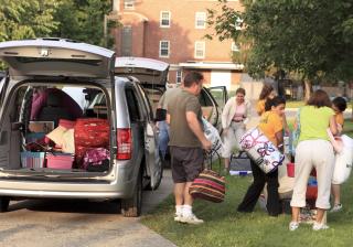 Family moving children into college, with the back of an SUV filled with boxes and clothes.