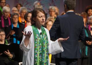 Rev. Mara Dowdall praying with closed eyes in front of GA choir
