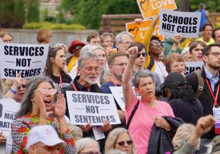 Protesters hold signs "Services not Sentences" and "Schools not Cells" at the General Assembly public witness event