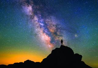 Stock photo of a figure silhouetted against a galaxy night sky.