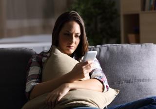 Sad girl reading phone message at home in the dark - Stock image