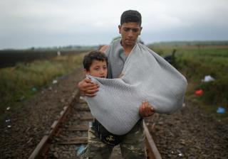 A youth carries a young boy in a makeshift sling as migrants walk towards waiting buses at the Hungarian border with Serbia on September 11, 2015 in Roszke, Hungary.