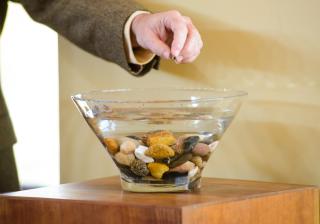 A hand placing a stone in a bowl of water.