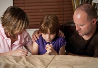 Child praying with mom and dad.