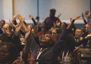 People raise their arms during a time of spiritual grounding at the BLUU Harper-Jones Theological Symposium on November 1