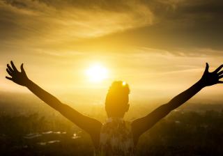 Black Girl Raising Arms over Valley in Sunset stock photo