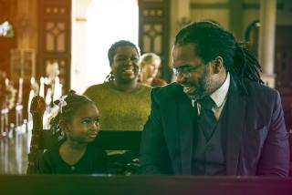 A Black father and young daughter looking happy at church with a smiling Black woman sitting in the row behind them. 