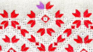 Red decorative stitching on white cloth with a small section of anomalous purple stitching