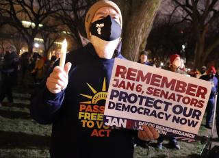 protester holding a candle and a sign that reads "remember Jan 7, senators, protect our democracy now"