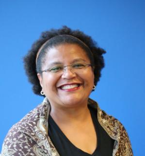 An African American woman wearing glasses and smiling against a blue background.