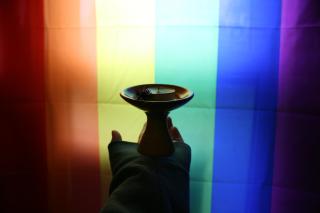 A chalice in front of an LGBTQIA+ rainbow flag, bordered by shadows.