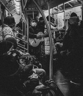 A man on a subway train masked and playing a guitar while onlookers watch.